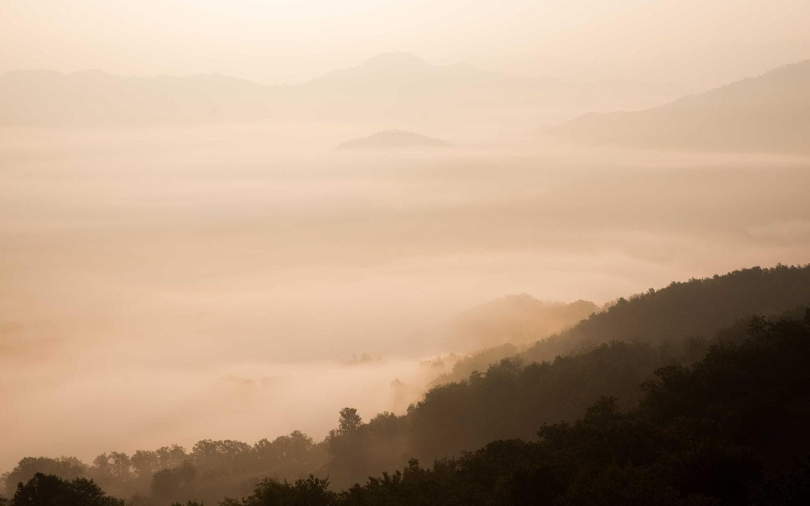 A lone hiker on a narrow ridge trail as morning mist clears from the valley below
